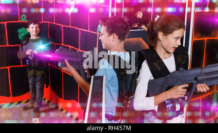 Allegro sorridenti teen ragazzo e una ragazza con pistole laser giocando tag laser con gli amici sul labirinto scuro Foto Stock