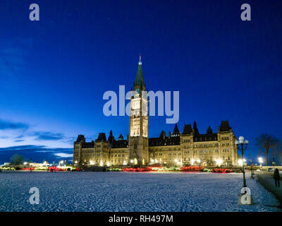 Del Canada agli edifici del Parlamento a notte: una visione illuminata del blocco centrale in una fredda notte d'inverno. C'è la neve su per la collina e la costruzione di riflettori contro un profondo cielo blu. Foto Stock