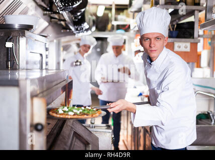 Ritratto di certi giovani chef lavorano nel moderno ristorante cucina, prepara la pizza fuori del forno Foto Stock