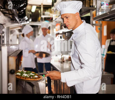 Ritratto di certi chef lavorano nel moderno ristorante cucina, prepara la pizza fuori del forno Foto Stock