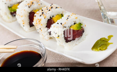 Tonno fresco e avocado uramaki sushi servita su piastra bianca con wasabi e salsa di soia Foto Stock