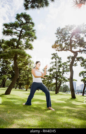 Donna pratica il tai chi nel soleggiato parco, Tokyo, Giappone Foto Stock