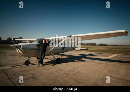 Ritratto fiducioso pilota maschio permanente al piccolo aereo ventilatore di sunny asfalto Foto Stock