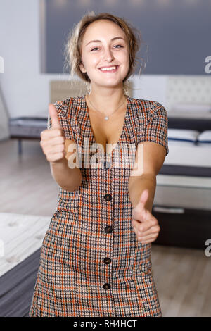 Allegro giovane donna dando pollice in alto come segno di acquisto di successo del nuovo materasso in negozio Foto Stock