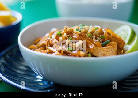 Ciotola di Pad Thai noodles con pollo, arachidi, cipolla verde e lime sul blu e le piastre bianche e colorate superficie verde. Foto Stock
