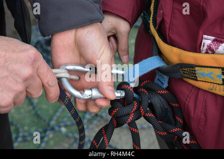 Vicino la mano di scalatore, alpinista, è regolazione ingranaggio di arrampicata, preparare le funi di sicurezza. Foto Stock