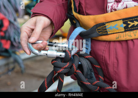 Vicino la mano di scalatore, alpinista, è regolazione ingranaggio di arrampicata, preparare le funi di sicurezza. Foto Stock