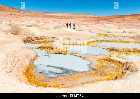 Tre i turisti a piedi dal fango box, fumarole e geyser di Sol de Manana vicino al sale di Uyuni piatto (Salar de Uyuni) nell'altipiano della Bolivia. Foto Stock