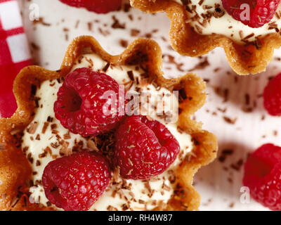 Il Brandy snap cesti riempiti con aroma di limone e crema guarnita con lamponi e scaglie di cioccolato Foto Stock