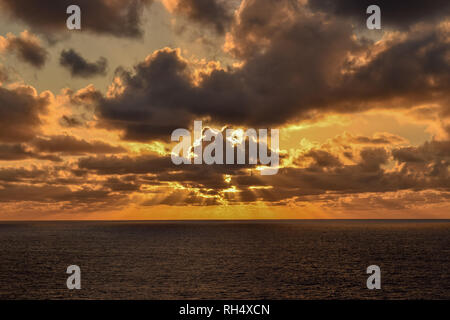 Gloriosa incandescente cielo arancione come sunray sparsi per l'orizzonte appena prima del tramonto sul Mar dei Caraibi su una sera Nuvoloso. Foto Stock