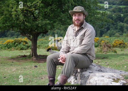 Giovani caucasici britannico escursionista seduto su un masso di granito da un albero di biancospino. Parco Nazionale di Dartmoor, Devon, Regno Unito. Foto Stock