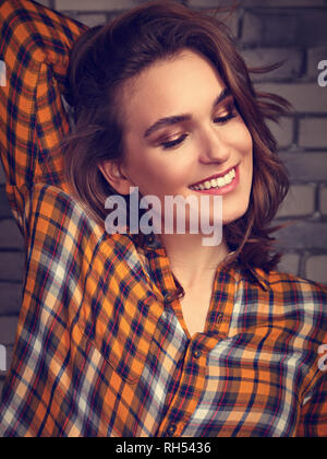 Bella toothy positivo donna sorridente cercando felice nel casual cella arancione sulla maglietta blu in mattoni di sfondo per studio. Closeup tonica ritratto Foto Stock