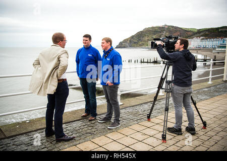 Media di trasmissione nel Regno Unito: una televisione BBC reporter e cameraman intervistando twoo giovani uomini sul lungomare di Aberystwyth, Wales UK Foto Stock