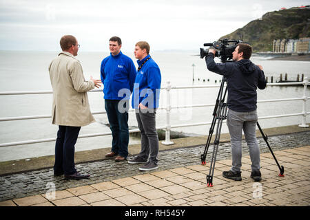 Media di trasmissione nel Regno Unito: una televisione BBC reporter e cameraman intervistando twoo giovani uomini sul lungomare di Aberystwyth, Wales UK Foto Stock