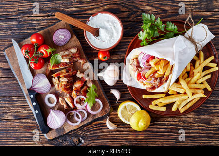 Souvlaki greco - pita wrap con grigliate di giroscopi rasata di carne, verdure, patatine fritte e yogurt salsa di aglio, ingredienti su di un bordo di taglio su un rusti Foto Stock