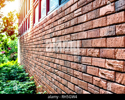 Muro di mattoni con il vetro della finestra vicino al giardino verde con la luce del sole. Vari pattern texture di mattoni rossi sulla parete. Foto Stock