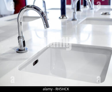 Acciaio inossidabile rubinetto sul lavello bianco decorazione in pubblico gli uomini bagno interno. Foto Stock