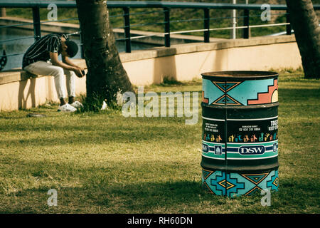 Durban, Sud Africa - Gennaio 6th, 2019: un decorato nel cestino della spazzatura figliata prossima ad una locale uomo seduto che un riposo all'aperto a Durban, Sud Africa. Foto Stock