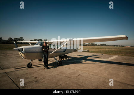 Pilota maschio permanente al piccolo aereo ventilatore di sunny asfalto Foto Stock