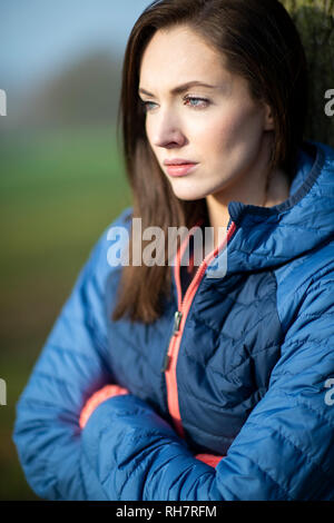 Cerca infelice giovane donna appoggiata ad albero sulla Passeggiata invernale nel Parco Foto Stock