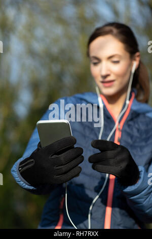 Giovane Donna scelta di musica da ascoltare sul telefono cellulare prima di esercitare in posizione di parcheggio Foto Stock