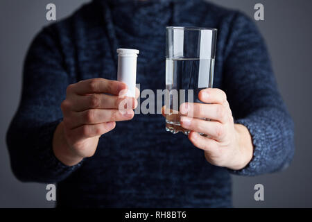 Maschio pronto a sciogliere la pillola in acqua. Solubile pillola bianca e un bicchiere di acqua nelle sue mani. Compressa effervescente aspirina in un bicchiere di acqua Foto Stock