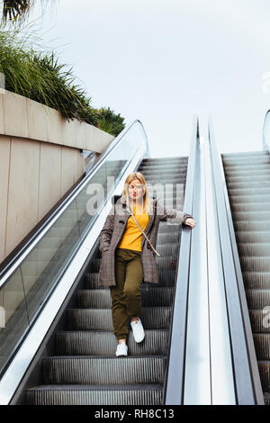 Ragazza bionda scendendo le scale mobili in centro commerciale Foto Stock