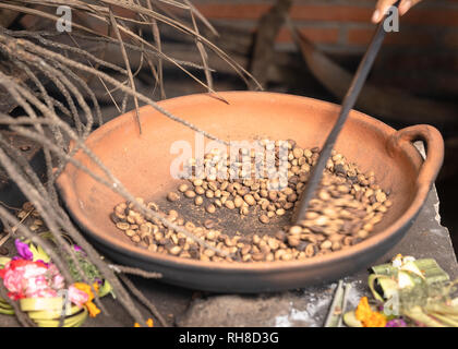 Tradizionali di chicchi di caffè La tostatura in una padella, la mano che regge un attrezzo di agitazione per spostare i fagioli. La tradizione di Bali. Motion Blur. Foto Stock