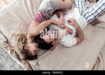 Bello dai capelli scuri Giovane Uomo in camicia bianca e il suo grazioso bionda moglie rimanere nel letto Foto Stock