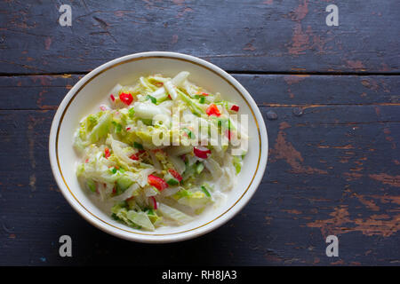 Insalata di verdure fatta di cavoli freschi, rafano, cetriolo, peperone e panna acida in una piastra bianca su una vecchia tavola nera. Vista dall'alto ingrandimento. Copia spa Foto Stock