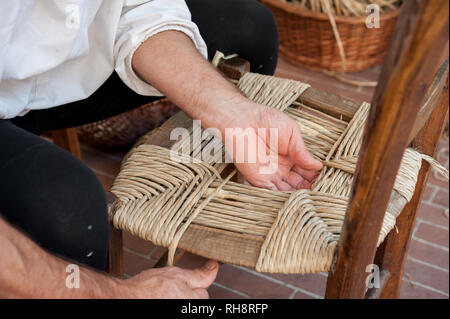 Un mender di sedie durante la riparazione di una sedia con sedile in paglia. Foto Stock