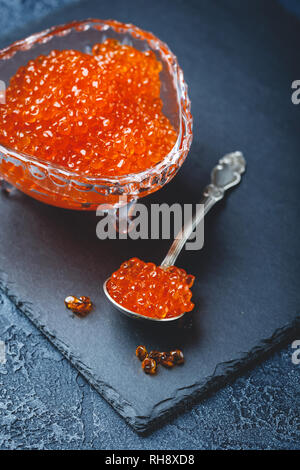 Salmone caviale rosso in lastra di cristallo con cucchiaio su sfondo nero. La squisita delicatezza Foto Stock