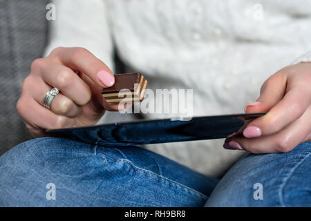 Ragazza con cioccolato e caramelle piastra in mani sulle ginocchia nel letto di casa. Sweet Food concept. Close up, il fuoco selettivo Foto Stock