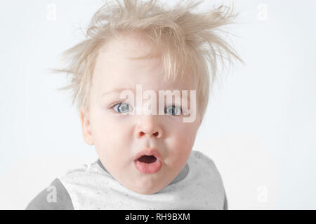 Carino sleepy disheveled baby sbadigli guardando la telecamera. Foto Stock