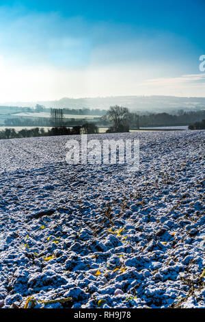 La mattina presto vista invernale, in una giornata di sole su una coperta di neve campo arato in lontane Misty Hills in Cotswolds, Gloucestershire, Regno Unito Foto Stock