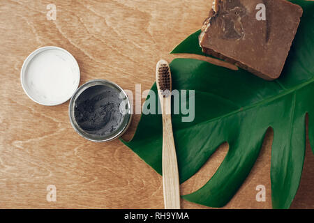 Dentifricio naturale il carbone attivato e bambù su uno spazzolino da denti in legno con sfondo verde foglia di monstera. Plastica bellezza gratuito essentials, cura dei denti. Foto Stock