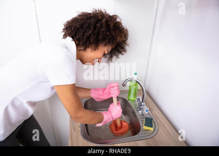 Close-up di un idraulico femmina indossando guanti di Rosa utilizzando lo stantuffo nel lavello da cucina Foto Stock