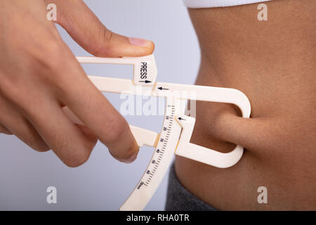 Close-up di una donna di mano la misurazione del lardo ventre con calibro su sfondo bianco Foto Stock
