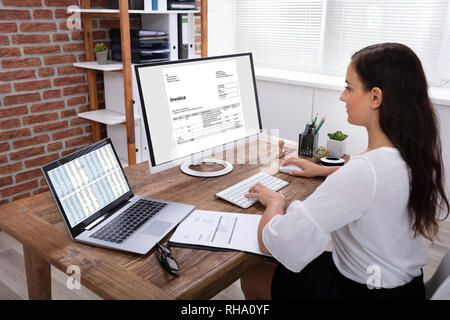 Giovane imprenditrice guardando la fattura sullo schermo del computer in ufficio Foto Stock