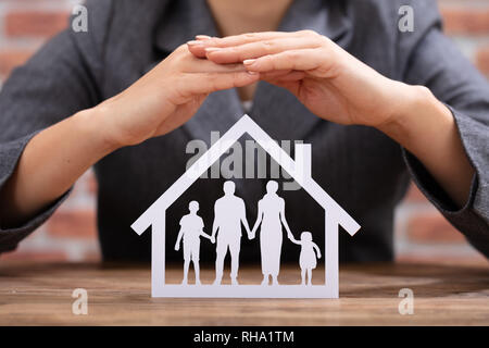 Close-up di una imprenditrice della protezione della famiglia carta tagliato con le mani sulla scrivania in legno Foto Stock