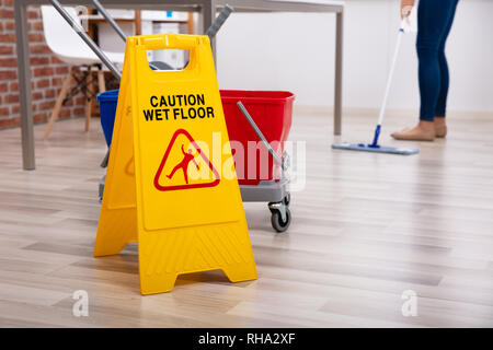 Sezione bassa di detergente per femmina in piedi in ufficio con Mop e segnale di avvertimento pavimento bagnato Foto Stock