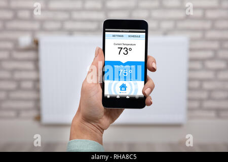 Close-up di Donna a mano la temperatura di impostazione del termostato usando applicazione Smartphone a casa Foto Stock