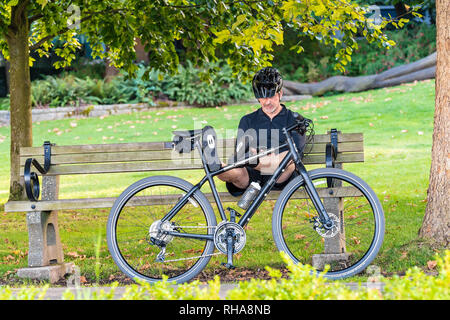 Vancouver, Canada - 23 Settembre 2017: Caucasica metà maschio 50s metà 60s in tutti vestiti di nero e casco seduto su una panchina nel parco con piedi distese sul Foto Stock