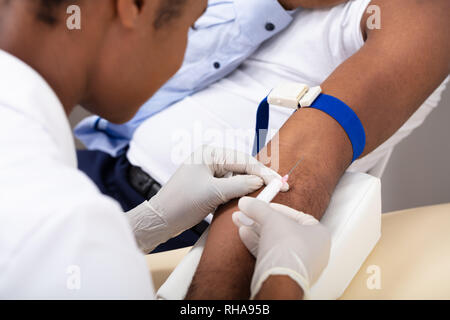 Close-up di medico donna iniettando il paziente di sesso maschile con siringa per raccogliere il campione di sangue Foto Stock