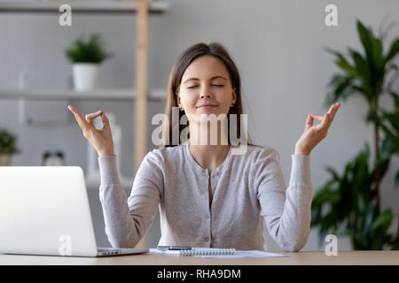 Calma giovane donna prendendo break facendo esercizi yoga al lavoro Foto Stock