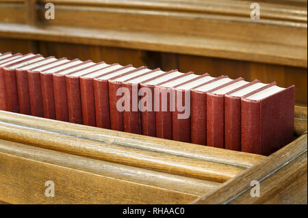Primo piano di una fila di red inno libri su una vecchia chiesa di legno pew. La illustra la religione e la preghiera Foto Stock