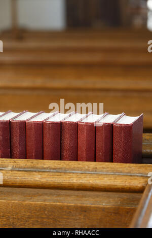 Dettaglio di una chiesa interno, una fila di red inno libri su una chiesa pew. La illustra la religione e la preghiera Foto Stock