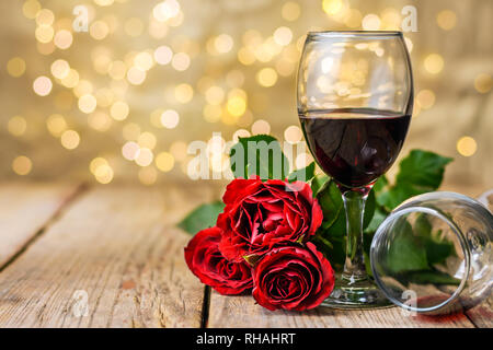 Il giorno di San Valentino ancora in vita. Due bicchieri di vino e rose rosse su una tavola in legno rustico di fronte a sfocare lo sfondo luminoso. Messa a fuoco selettiva. Foto Stock