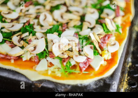 Processo di fabbricazione di pizza. Italiano di salsiccia per pizza pizza con funghi, rucola, pomodori, mozzarella, aglio e salsa Foto Stock