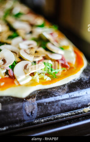Processo di fabbricazione di pizza. Italiano di salsiccia per pizza pizza con funghi, rucola, pomodori, mozzarella, aglio e salsa. Salsiccia per pizza pizza sul vassoio da forno Foto Stock